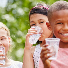 3 crianças sorridentes com um copo de água na mão