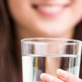 imagem de uma mulher segurando um copo de agua e sorrindo