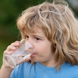 Imagem criança bebendo agua em copo de vidro ao ar livre